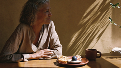 Woman in her 50s with silver hair enjoying a calm breakfast of figs and toast in warm morning light