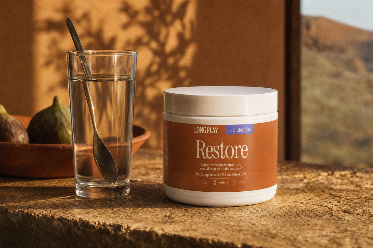 Longplay L-Glutamine Powder tub next to a glass of water on a sandstone kitchen counter