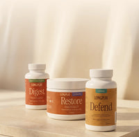 Three LongPlay supplement containers on a light stone surface against a soft cream backdrop: a Digest bottle, a Restore jar, and a larger Defend bottle.