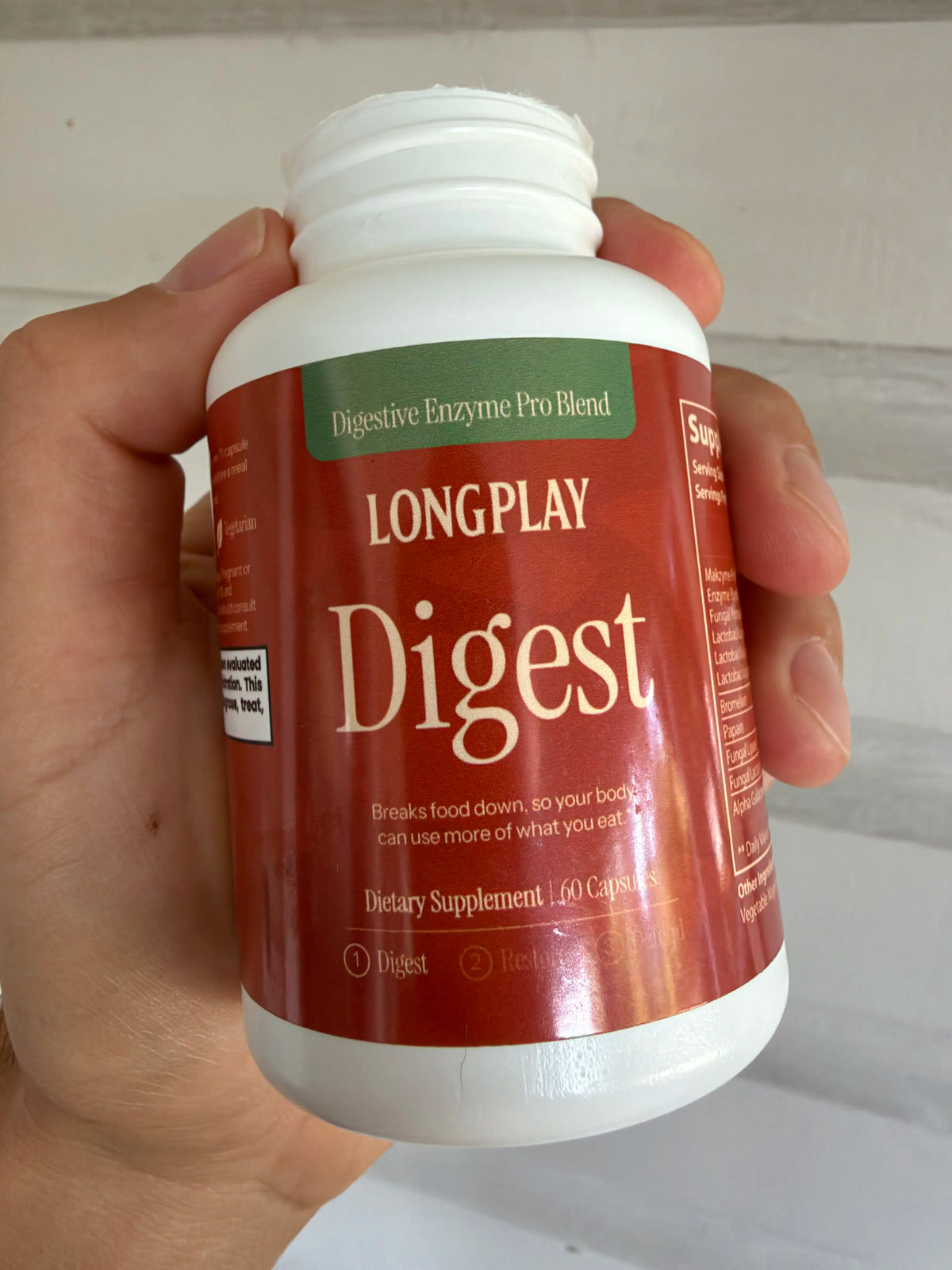 A hand holding a bottle of Longplay Digest digestive enzyme supplement